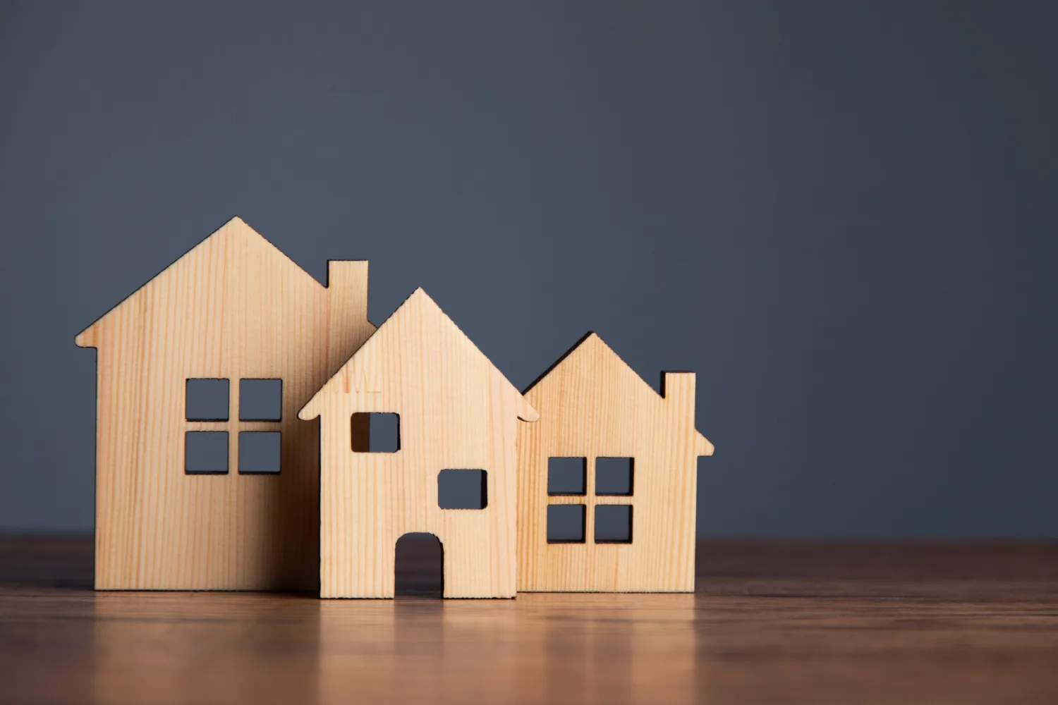 3 petites maison en bois posé sur un plan de travail sur fond gris